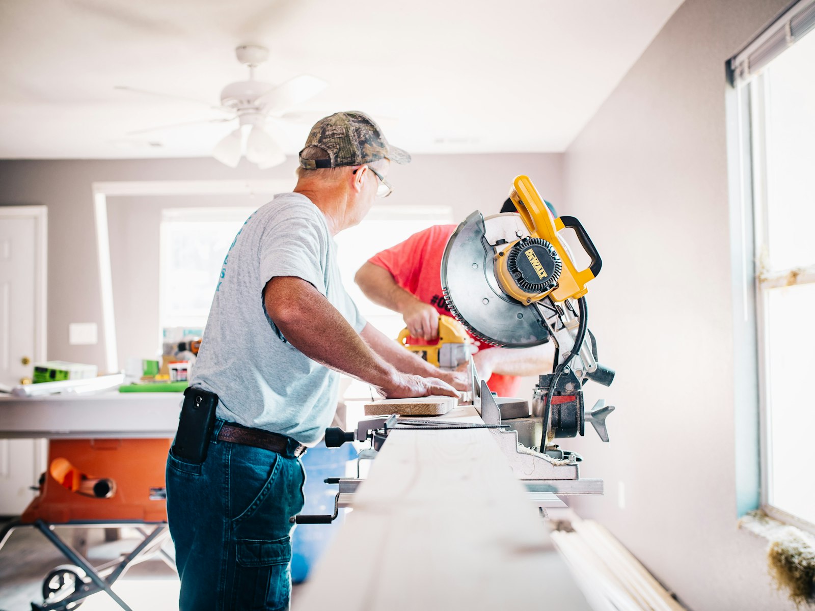 Renovation crew cutting trim with a miter saw inside a home under renovation